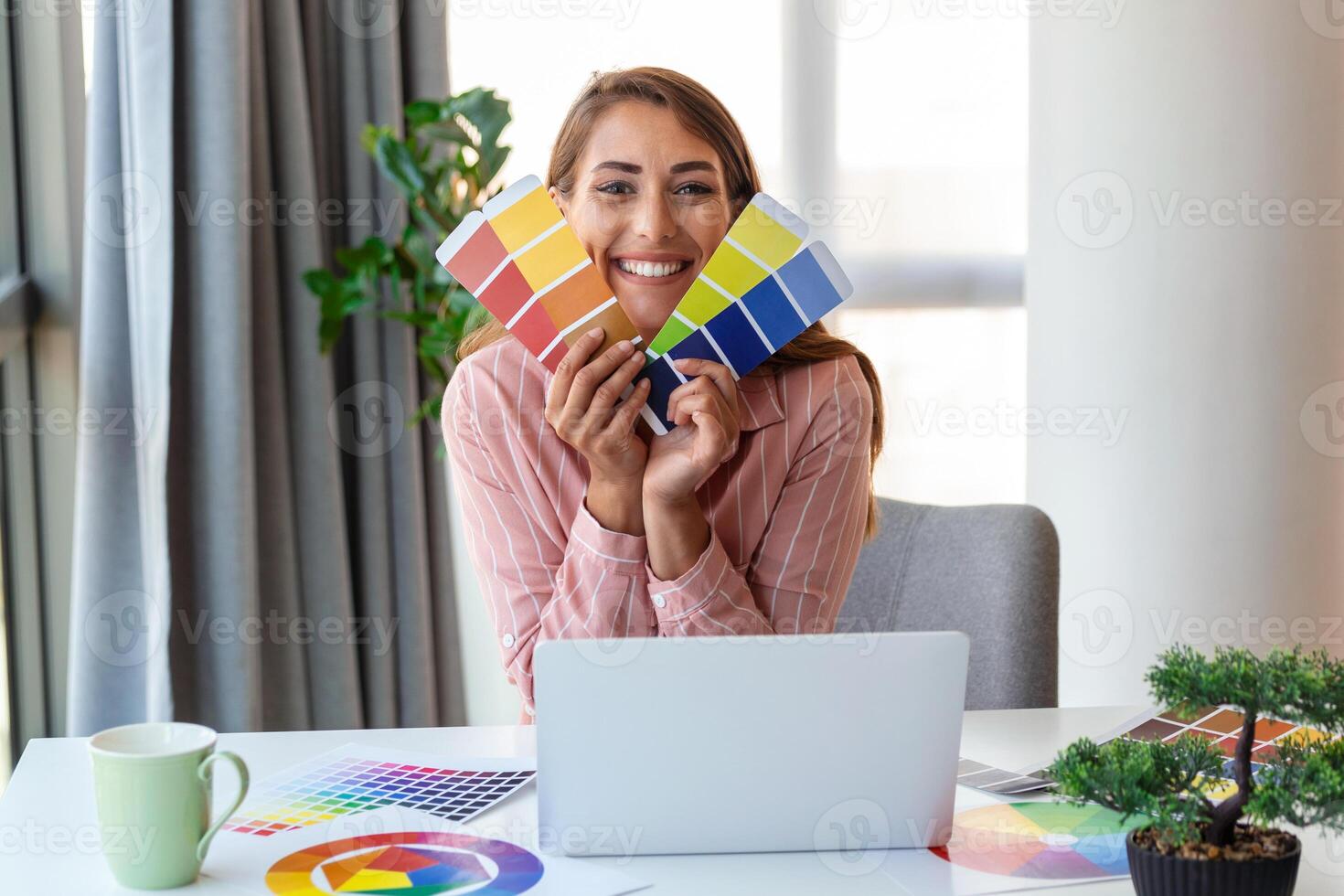 Cheerful youn woman designer having video conference with clients, sitting at desk in front of computer, holding color palettes, gesturing and smiling, copy space photo