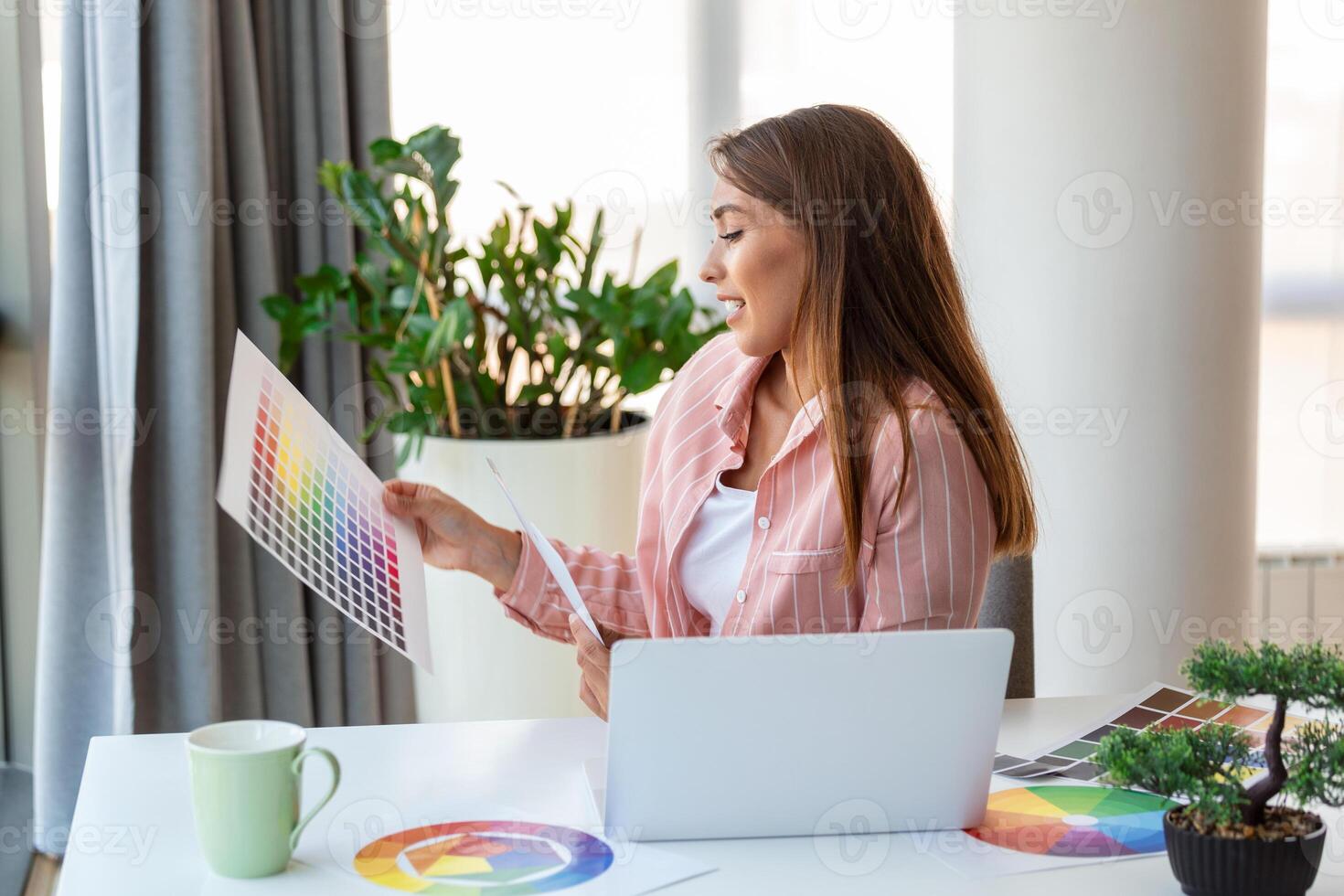 Cheerful youn woman designer having video conference with clients, sitting at desk in front of computer, holding color palettes, gesturing and smiling, copy space photo