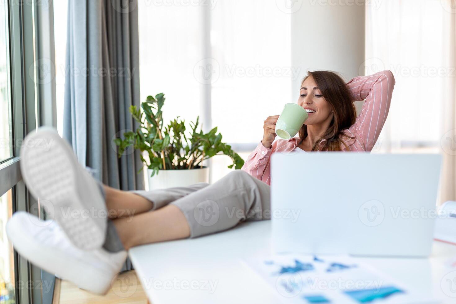 Young pretty businesswoman in the office sitting in office chair, hands up and with her feet up on a desk enjoying coffee photo