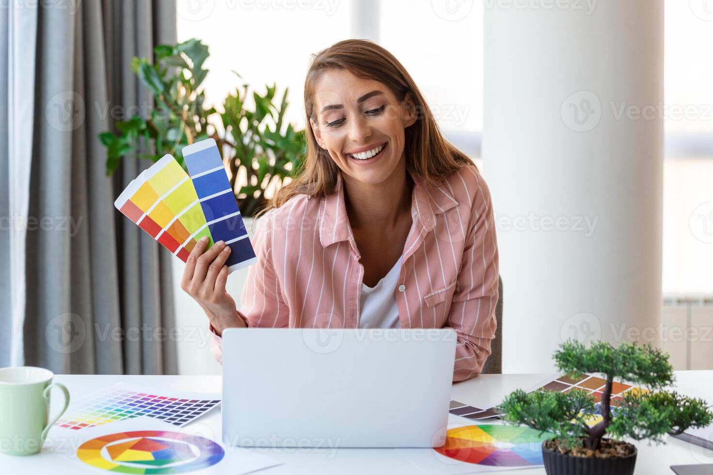 Cheerful youn woman designer having video conference with clients, sitting at desk in front of computer, holding color palettes, gesturing and smiling, copy space photo