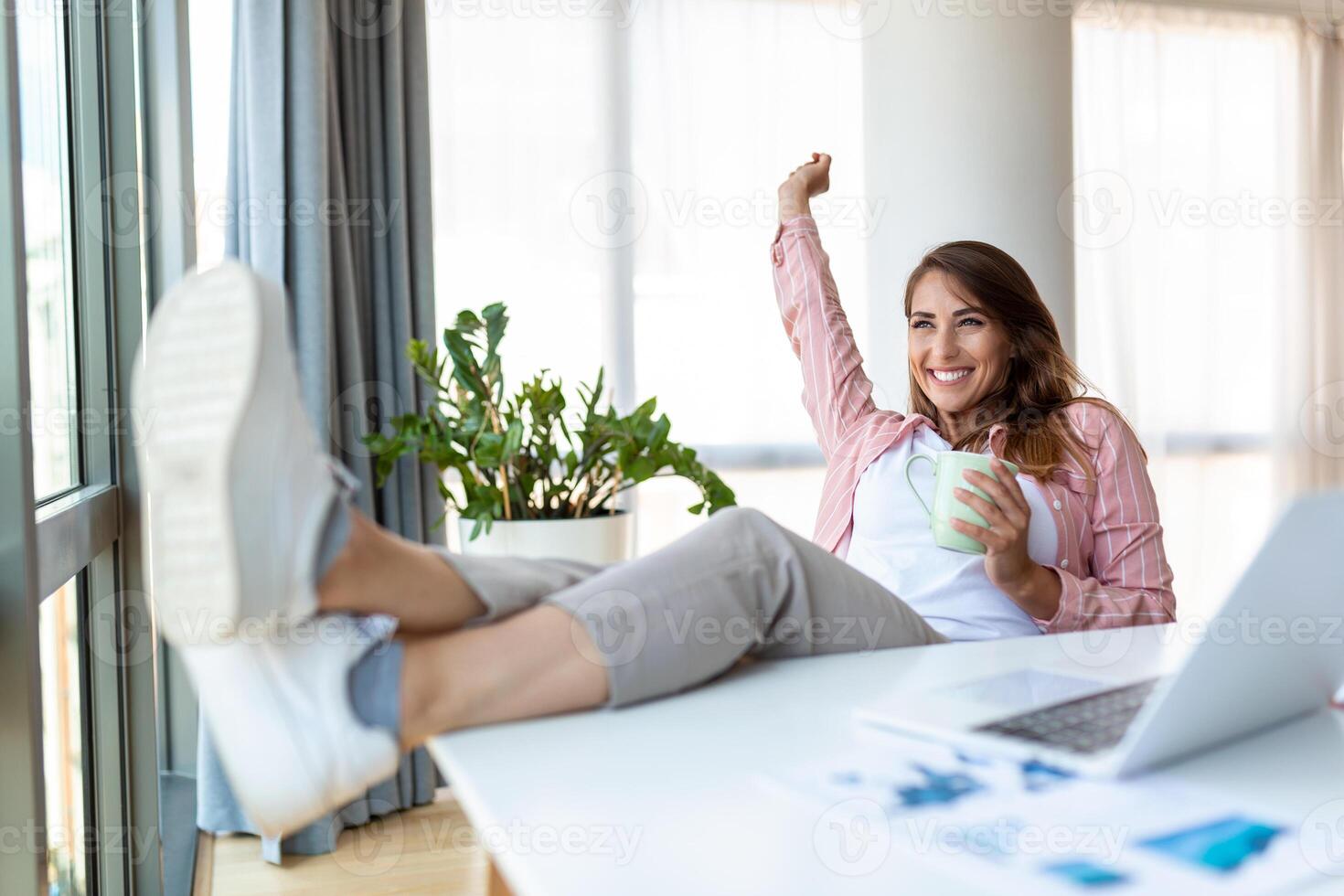 Young pretty businesswoman in the office sitting in office chair, hands up and with her feet up on a desk enjoying coffee photo