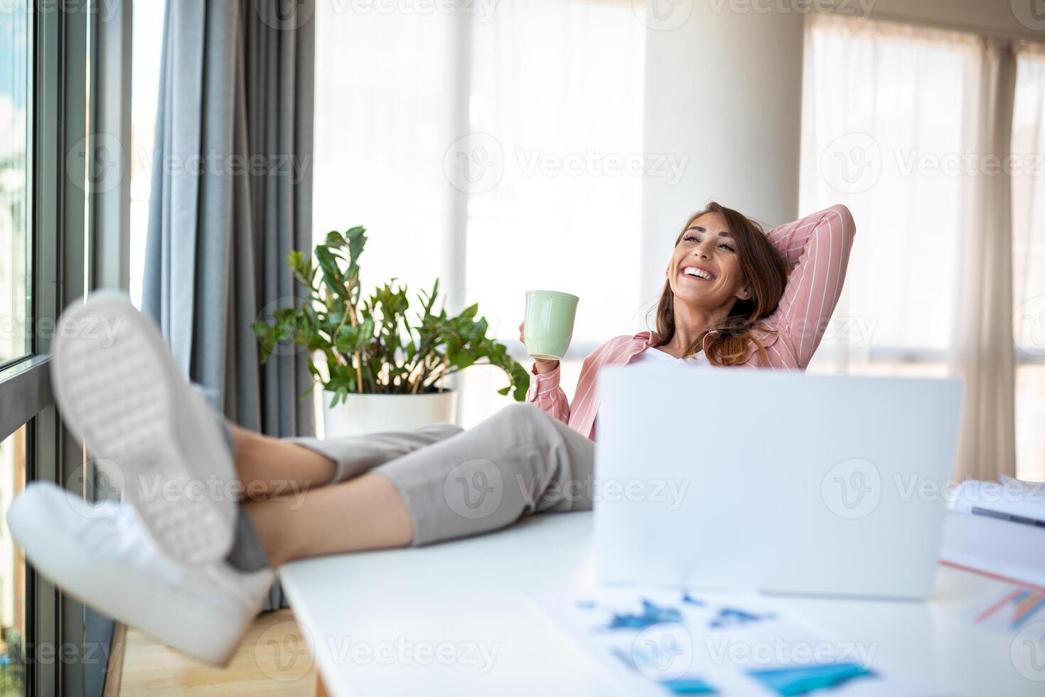 Young pretty businesswoman in the office sitting in office chair, hands up and with her feet up on a desk enjoying coffee photo