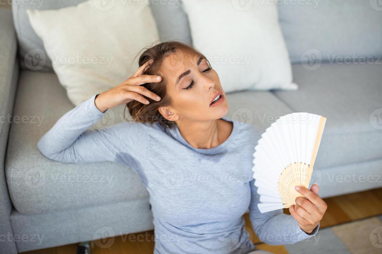 Woman puts head on sofa cushions feels sluggish due unbearable heat, waves hand fan cool herself, hot summer flat without air-conditioner climate control system concept photo