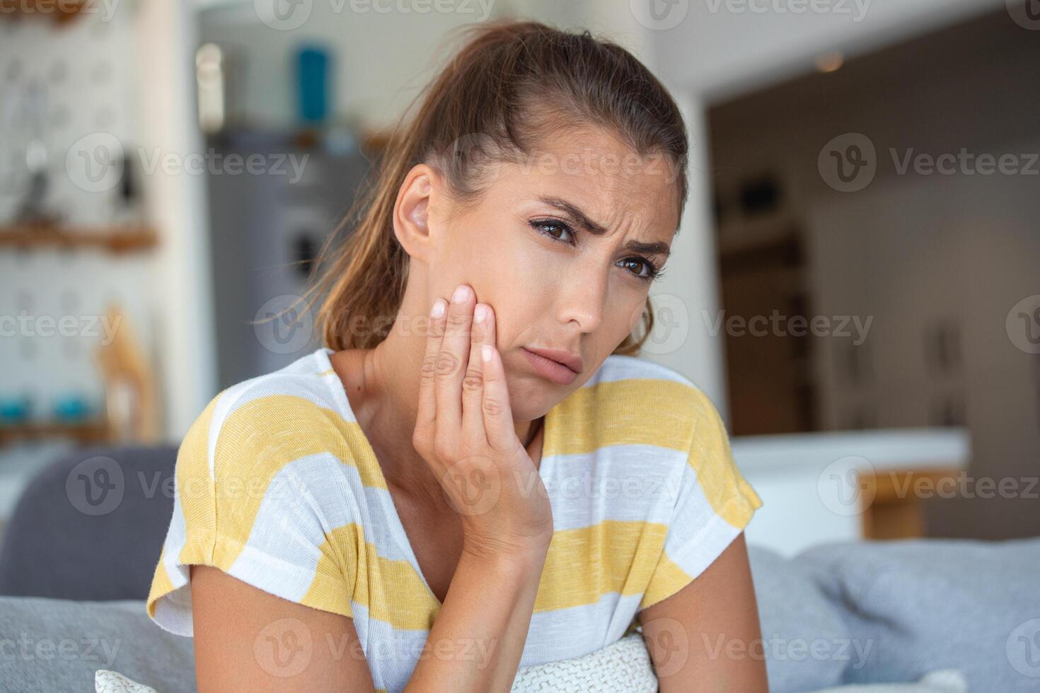 Portrait of unhappy young woman suffering from toothache at home. Healthcare, dental health and problem concept. photo