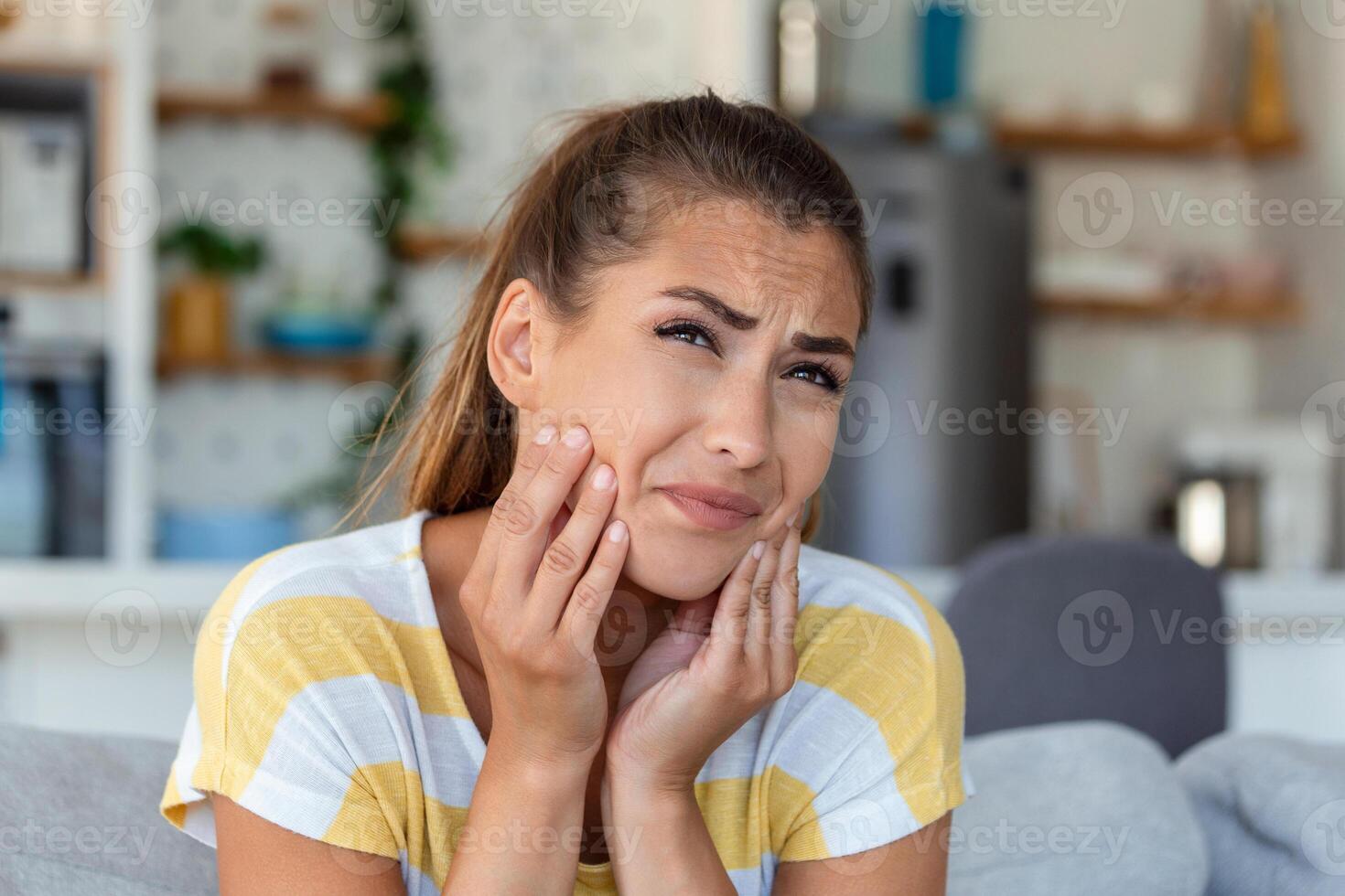 Portrait of unhappy young woman suffering from toothache at home. Healthcare, dental health and problem concept. photo