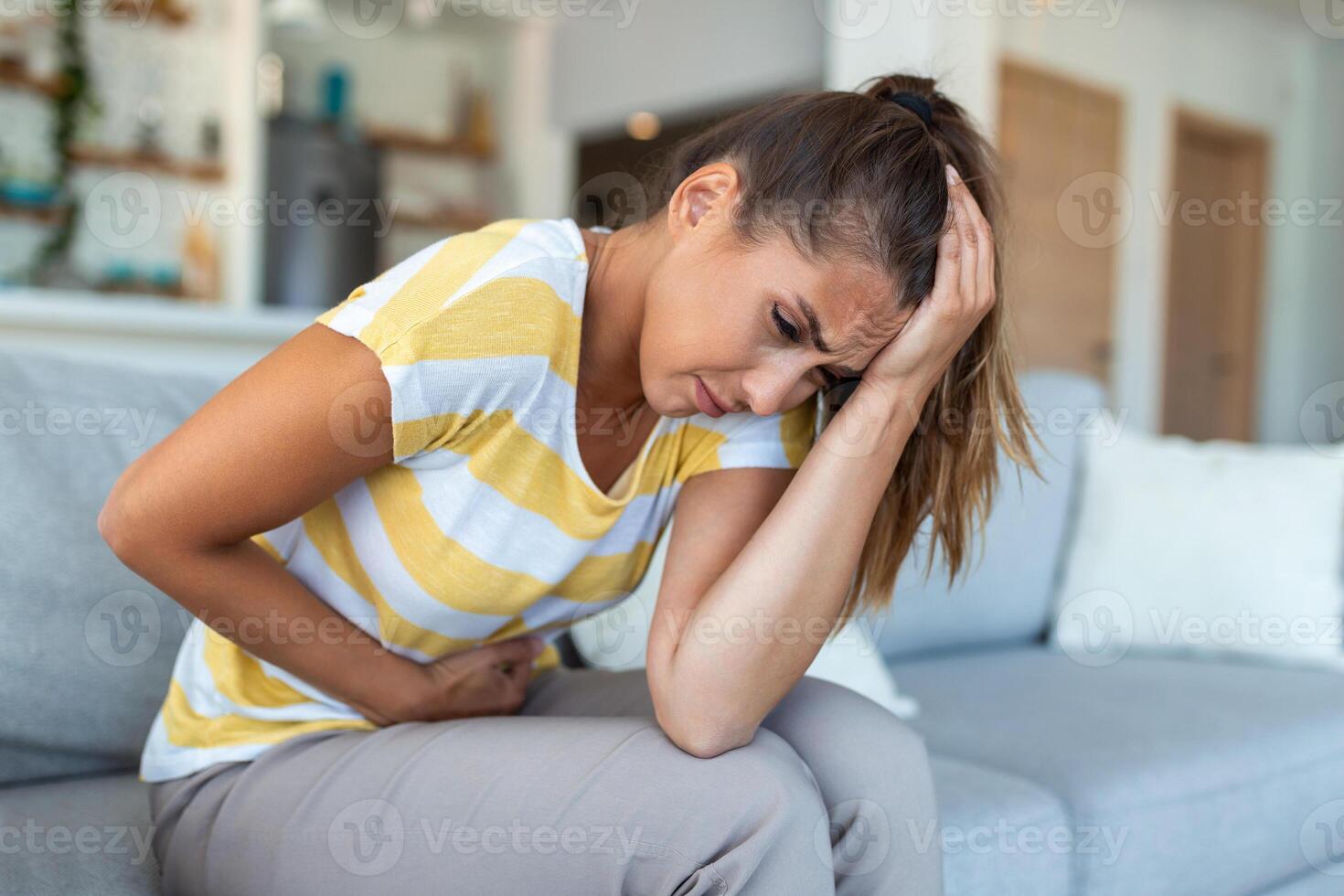 Woman lying on sofa looking sick in the living room. Beautiful young woman lying on bed and holding hands on her stomach. Woman having painful stomachache on bed, Menstrual period photo