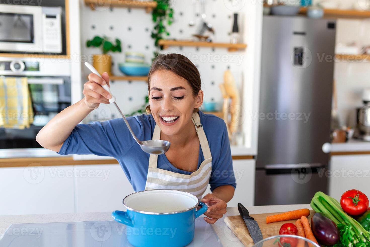 contento joven mujer Cocinando saboreo cena en un maceta en pie en moderno cocina a hogar. ama de casa preparando sano comida sonriente . casa y nutrición. dieta recetas concepto foto