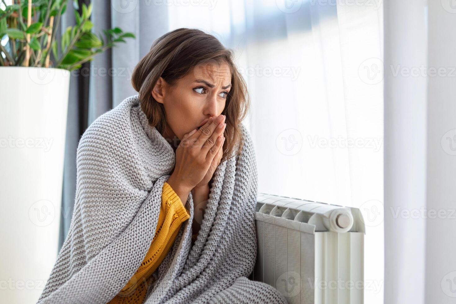 Woman freezing at home, sitting by the cold radiator. Woman with home heating problem feeling cold photo