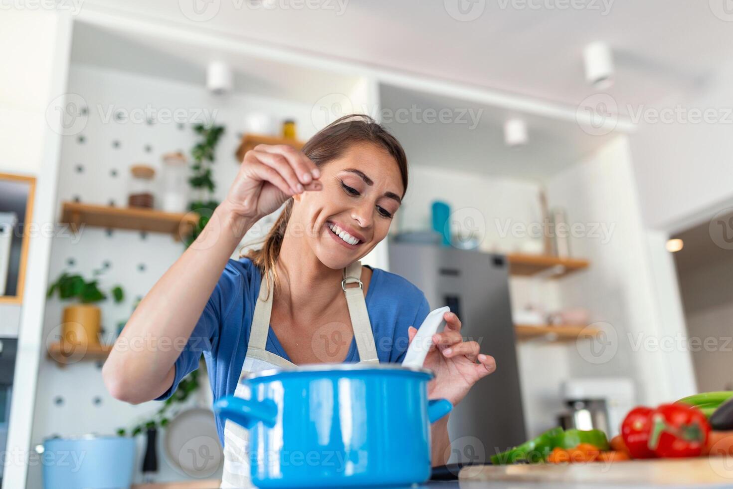 contento joven mujer Cocinando saboreo cena en un maceta en pie en moderno cocina a hogar. ama de casa preparando sano comida sonriente . casa y nutrición. dieta recetas concepto foto