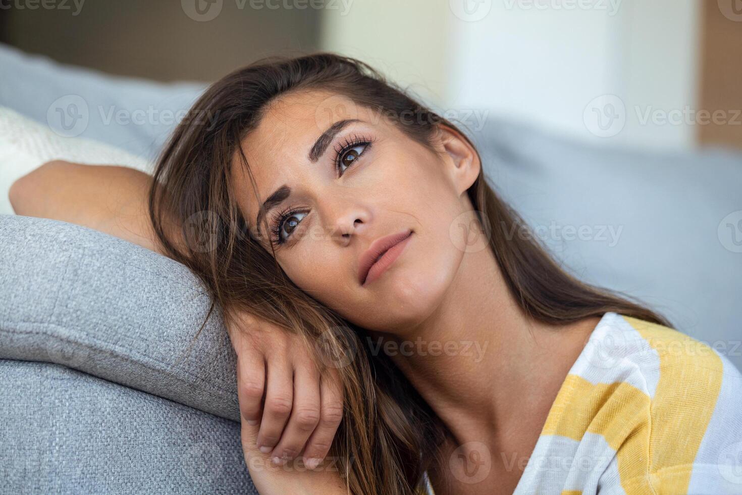 Happy young woman sitting on sofa at home and looking at camera. Portrait of beautiful woman smiling and relaxing during summer. photo
