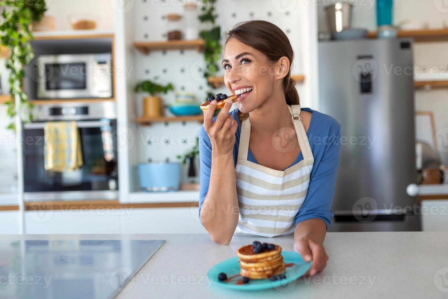 Young woman making pancakes at kitchen. Young housewife enjoying blueberry pancakes for breakfast photo