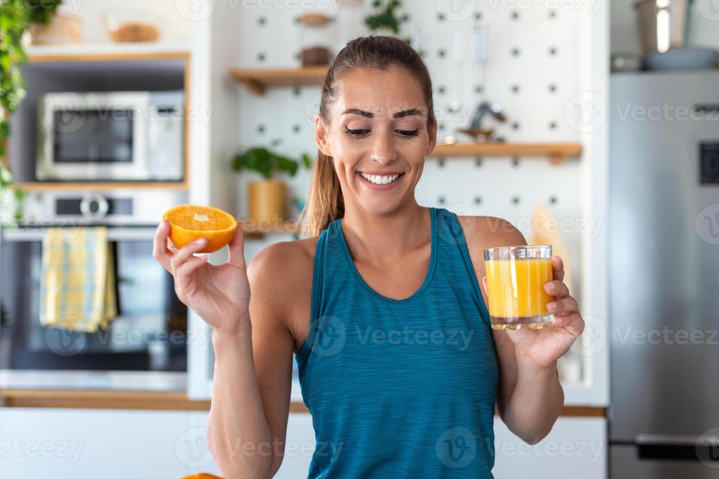 Beautiful young woman drinking fresh orange juice in kitchen. Healthy diet. Happy young woman with glass of juice and orange at table in kitchen. photo