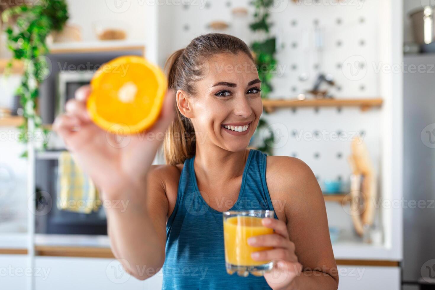 Beautiful young woman drinking fresh orange juice in kitchen. Healthy diet. Happy young woman with glass of juice and orange at table in kitchen. photo