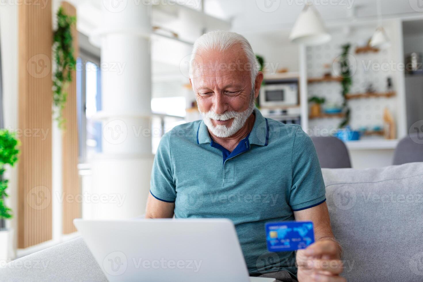 Mature man using laptop, holding plastic credit or debit card, senior grey haired customer making secure internet payment, shopping or browsing online banking service, entering information photo