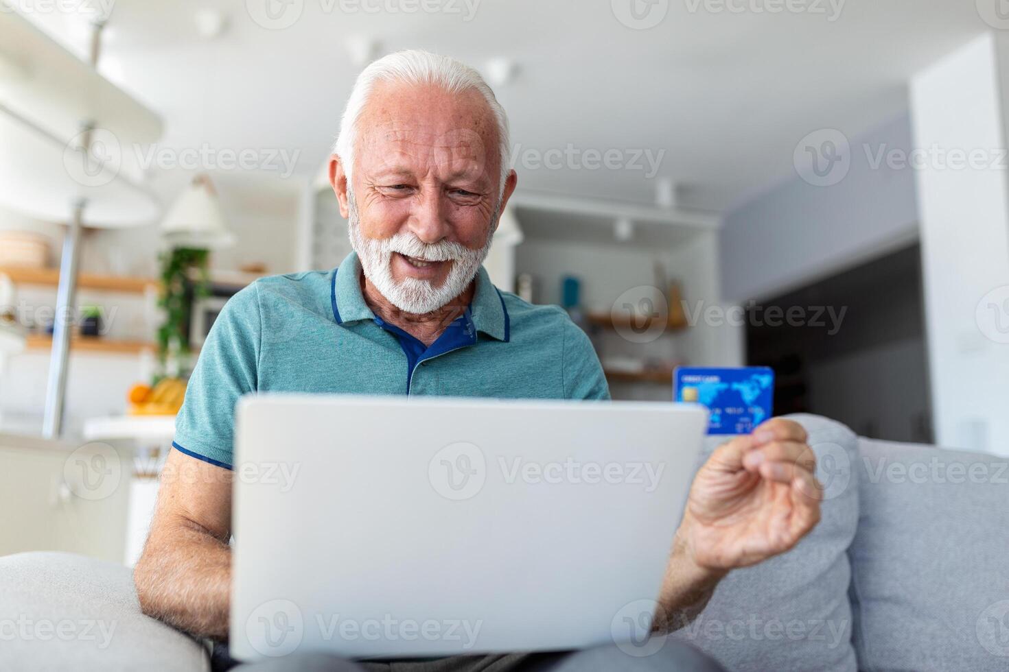 Mature man using laptop, holding plastic credit or debit card, senior grey haired customer making secure internet payment, shopping or browsing online banking service, entering information photo