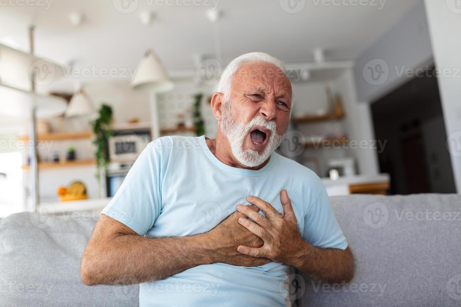 Senior man presses hand to chest has heart attack suffers from unbearable pain, Mature man with pain on heart in living room. Senior man suffering from bad pain in his chest heart attack at home photo