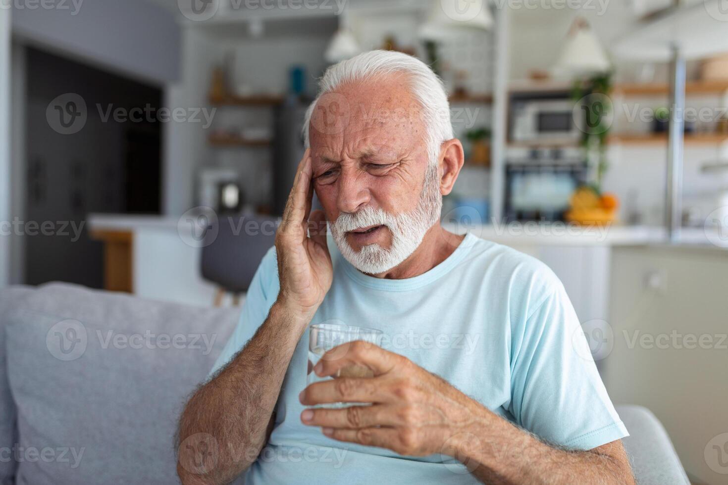 senior man suffering from a headache at home. Worried senior man sitting alone in his home. This headache really hurts. My head is killing me photo