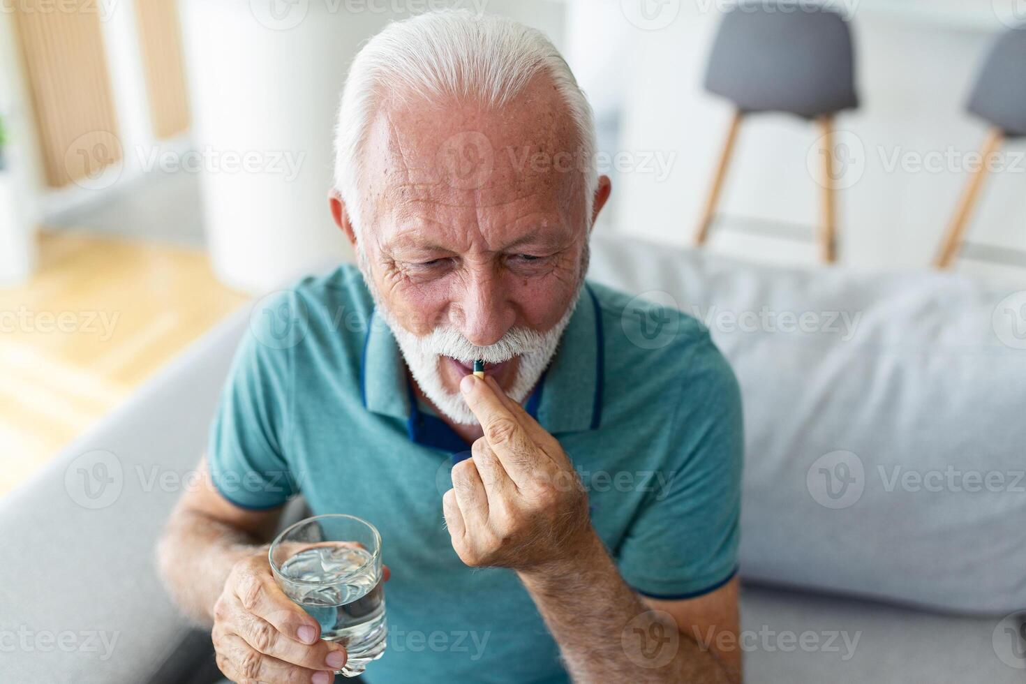 Senior man takes pill with glass of water in hand. Stressed mature man drinking sedated antidepressant meds. Man feels depressed, taking drugs. Medicines at work photo