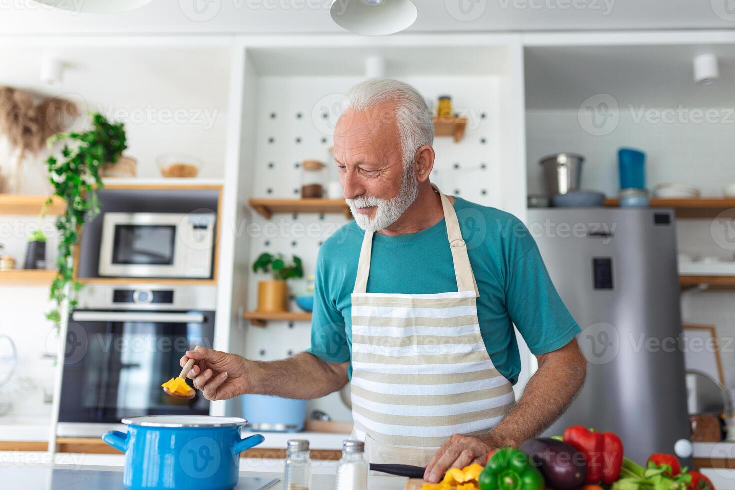 Happy senior man having fun cooking at home - Elderly person preparing health lunch in modern kitchen - Retired lifestyle time and food nutrition concept photo