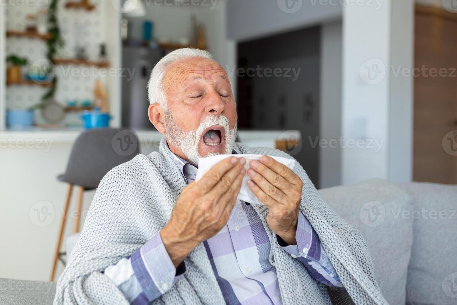 Mature man feeling sick with cold and fever at home, ill with flu disease sitting on the sofa with ice pack on his head photo