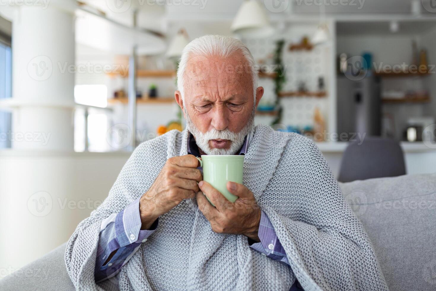 mayor hombre sufrimiento desde gripe Bebiendo té mientras sentado envuelto en un cobija en el sofá a hogar. enfermo hombre con un frío acostado en el sofá participación un jarra de caliente té. foto