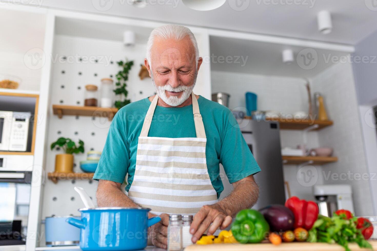 Happy senior man having fun cooking at home - Elderly person preparing health lunch in modern kitchen - Retired lifestyle time and food nutrition concept photo