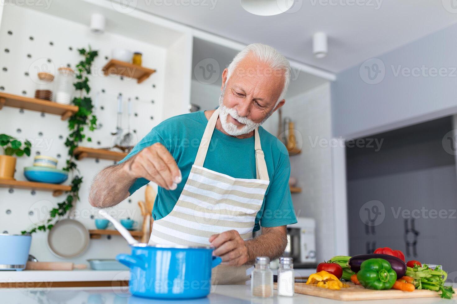 Happy senior man having fun cooking at home - Elderly person preparing health lunch in modern kitchen - Retired lifestyle time and food nutrition concept photo