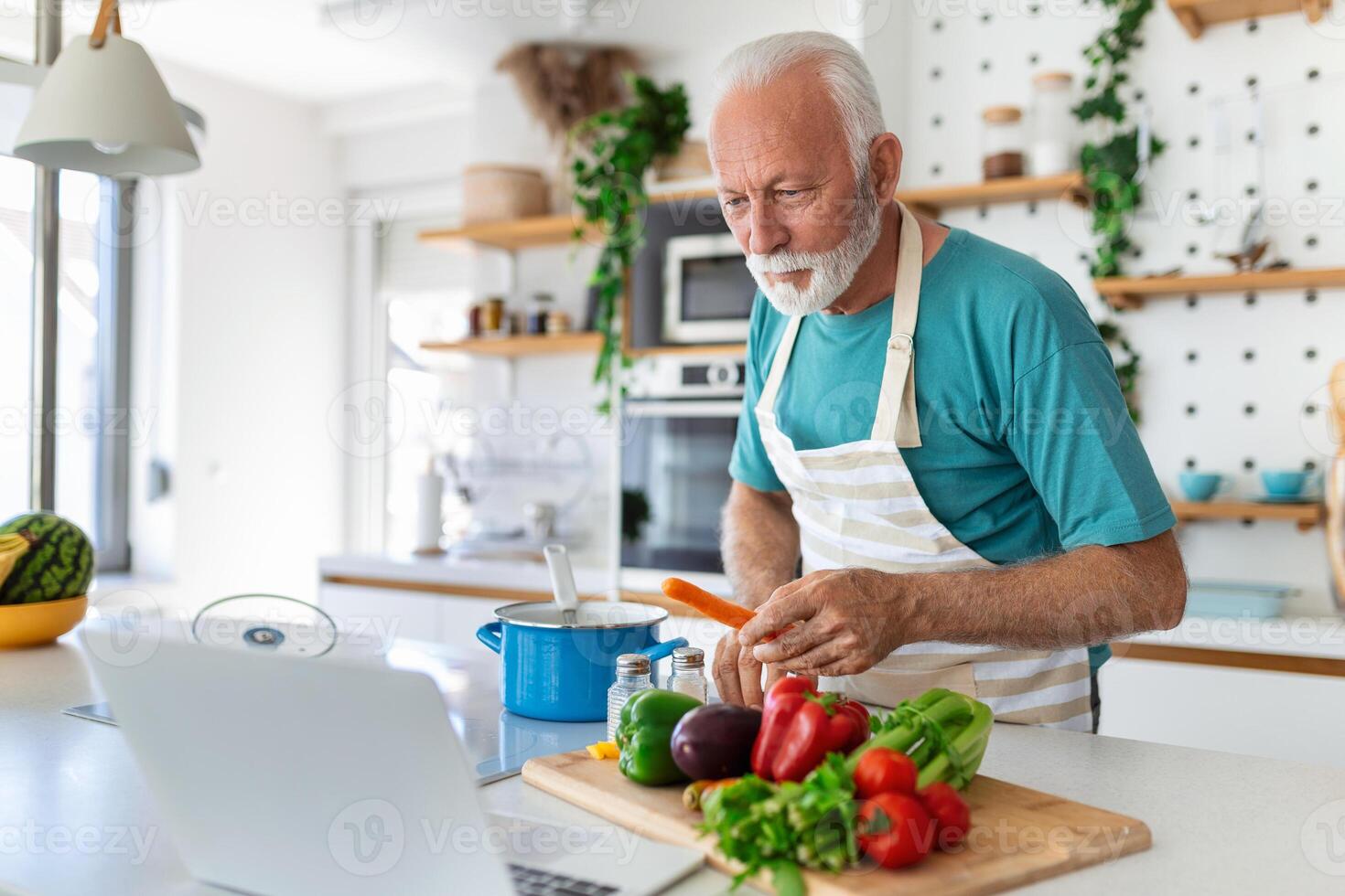 Happy senior man having fun cooking at home - Elderly person preparing health lunch in modern kitchen - Retired lifestyle time and food nutrition concept photo
