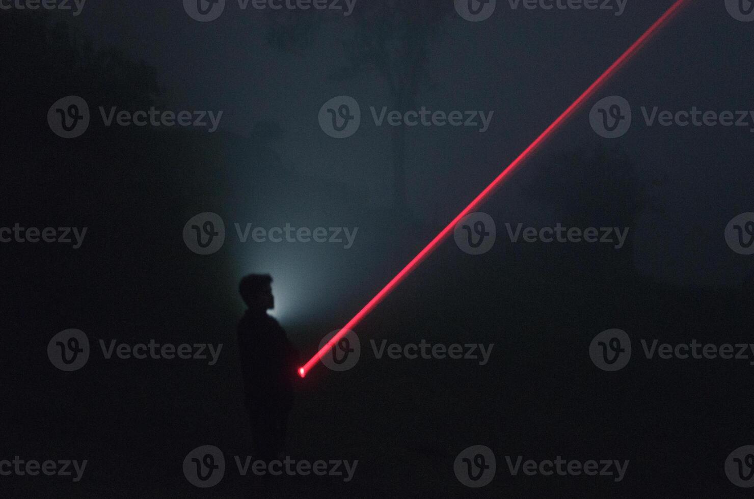 long exposure shot of silhouette of man holding a red laser photo