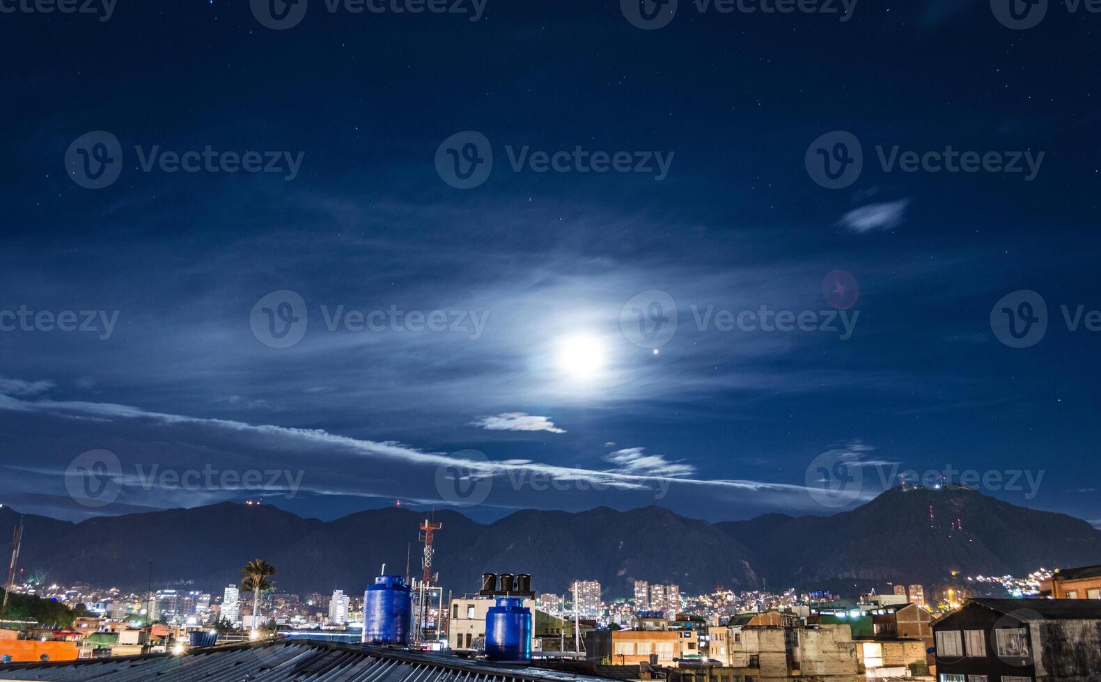 dramatic shot of cityscape at bogota with a full moon over the night sky over the hills photo
