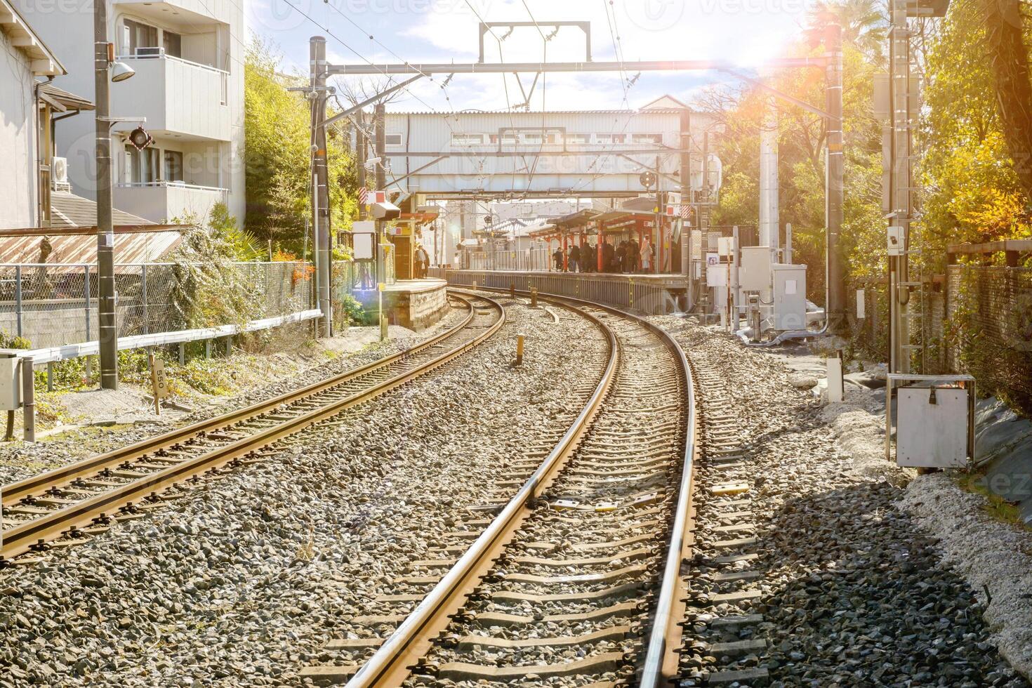 Metal and stoneware railroad tracks and cityscape with sun flare and blurry background of crowd people waiting train at train platform. photo