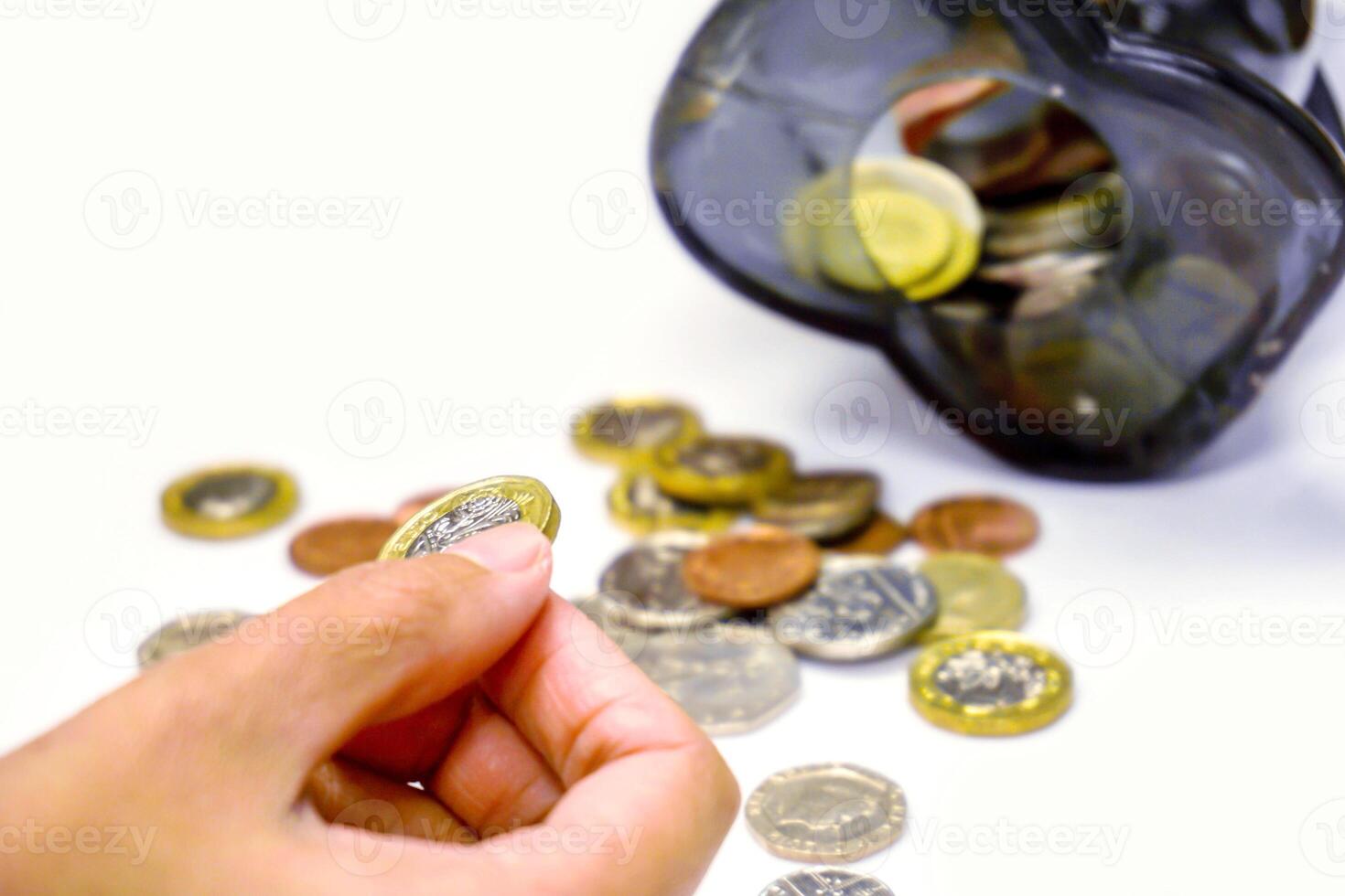Image of hand picking up a new one pound British currency coins on blurry coins open from the piggy bank laid out scattered on white background. photo