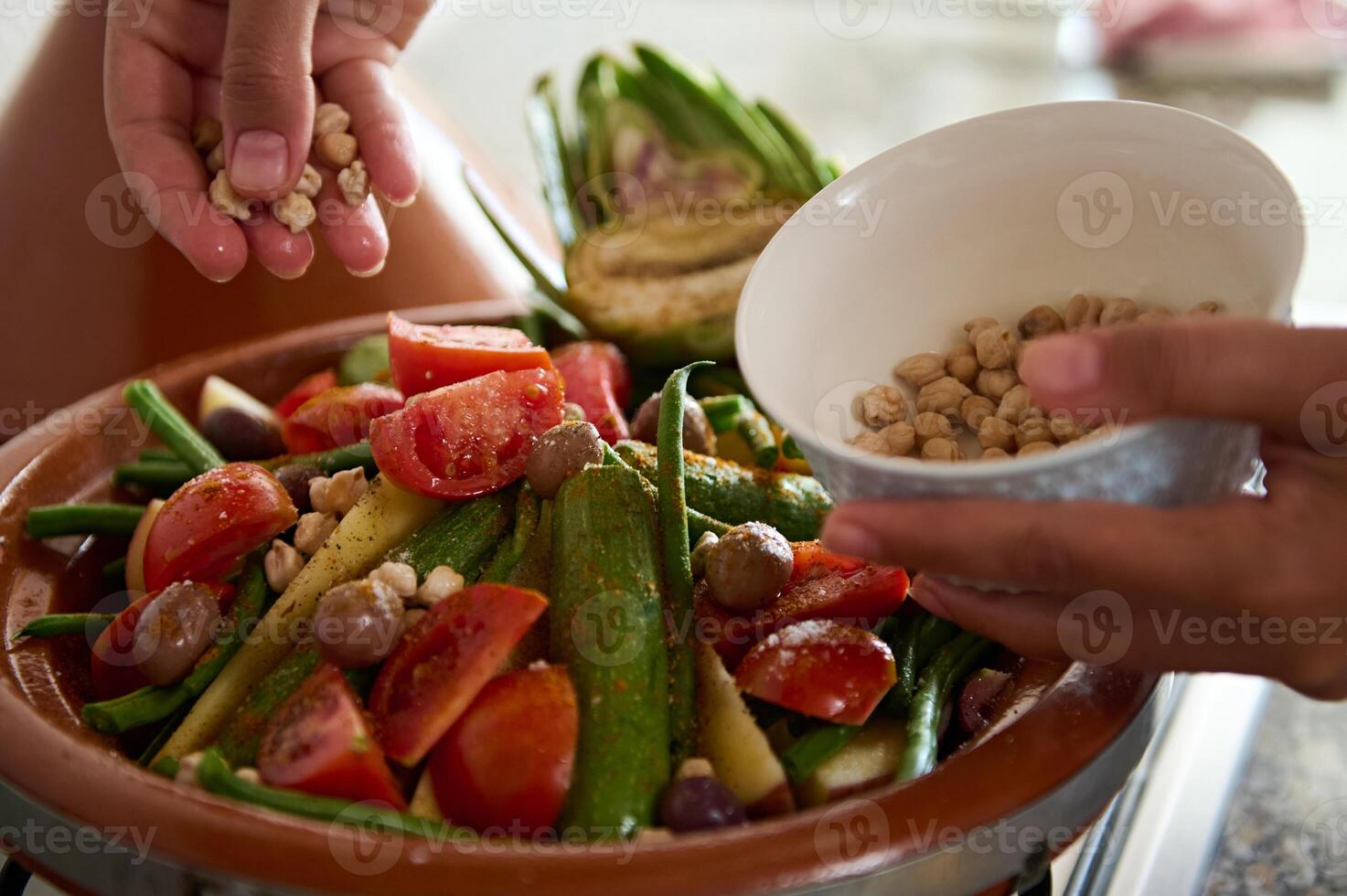Closeup of the hands of a housewife adding chickpeas into a meal while cooking healthy vegetarian meal in tagine photo