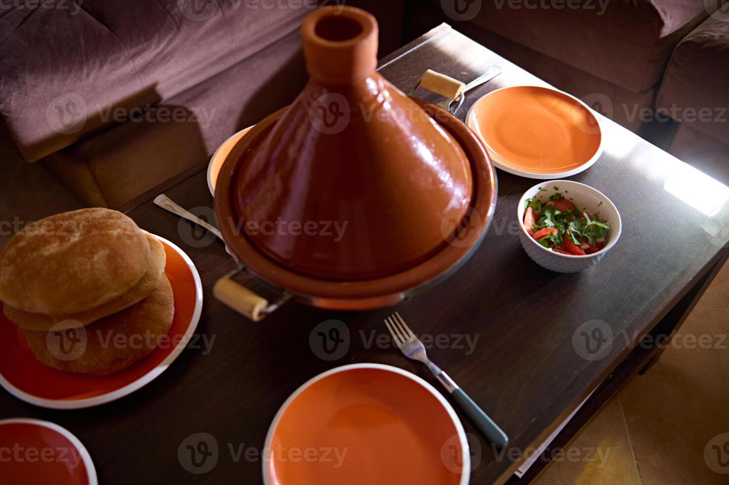 tradicional marroquí familia cena - sabroso comida cocido en tagine arcilla maceta con recién horneado un pan en el mesa a hogar foto