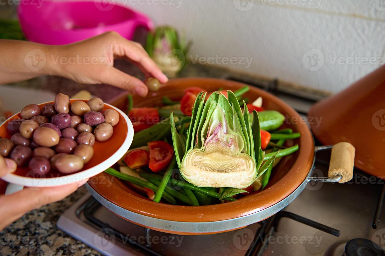 de cerca ama de casa agregando aceitunas dentro un comida mientras Cocinando sano vegetariano comida en tagine foto