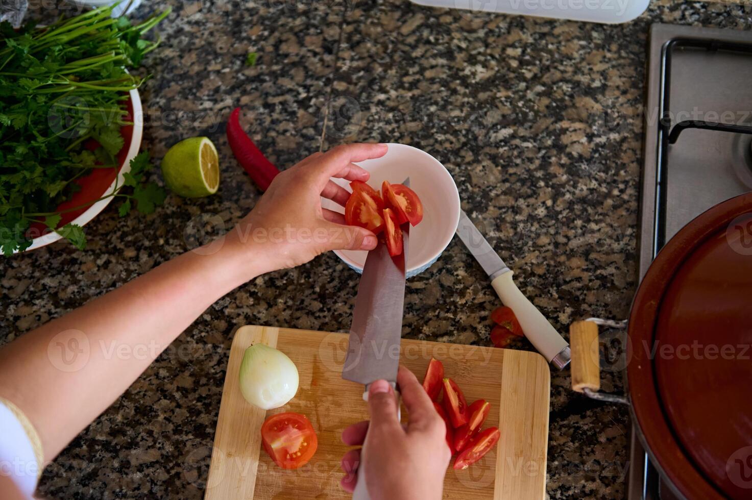 View from above of a chef slicing vegetables, adding chopped tomatoes into a white salad bowl photo