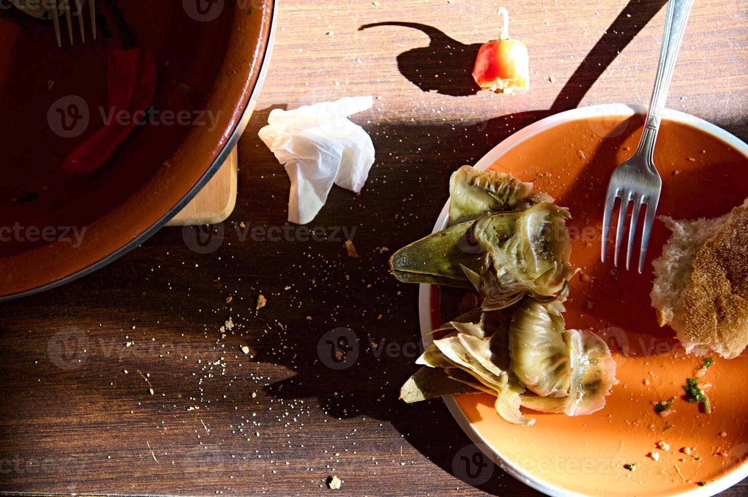 Top view dirty empty plate with bread crumbs and the rest of unfinished food near a clay tagine dish on a wooden table photo