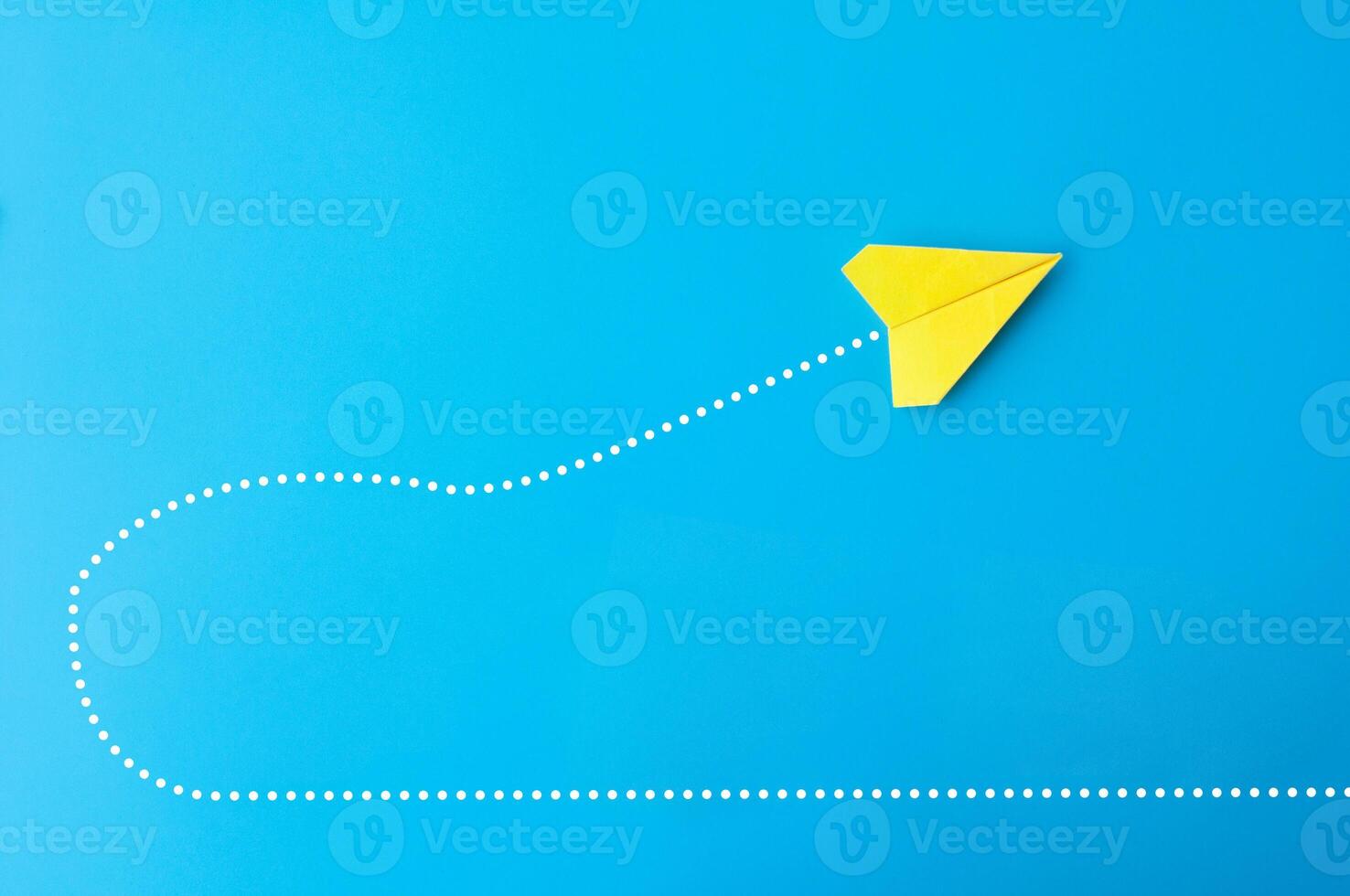 Top view of yellow paper airplane making a U turn on blue background photo