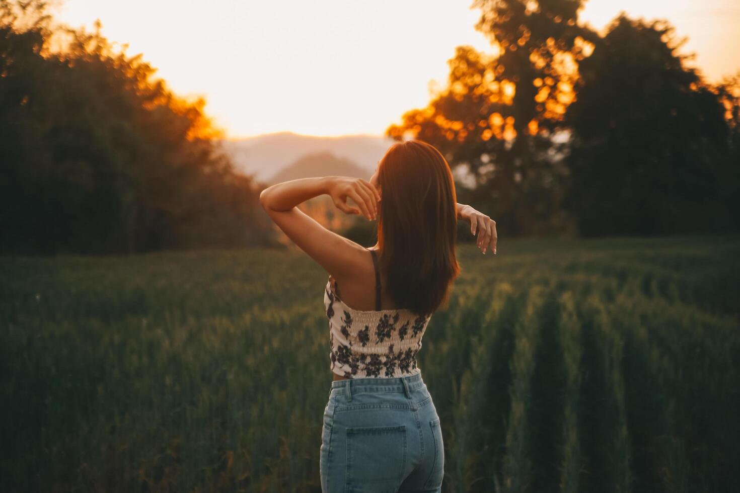 Young pretty woman in red summer dress and straw hat walking on yellow farm field with ripe golden wheat enjoying warm evening. photo