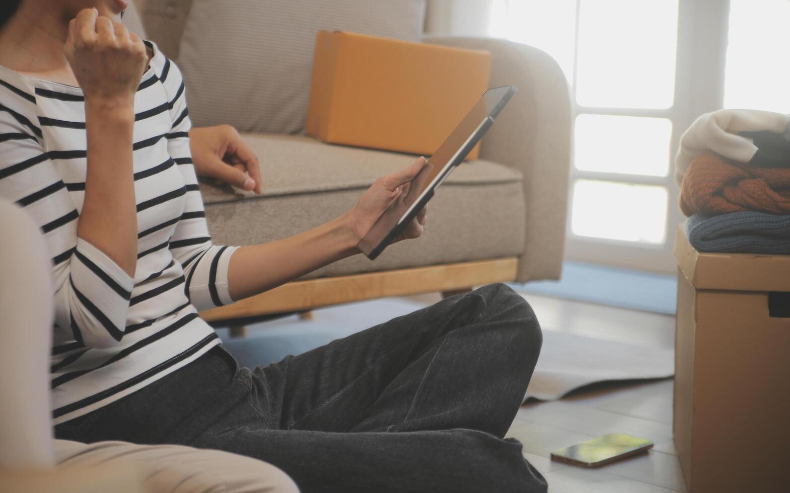 Two Asian blogger showing clothes in front of the camera to recording vlog video live streaming at her shop. Online Shopping Cart notion. on sofa at home photo
