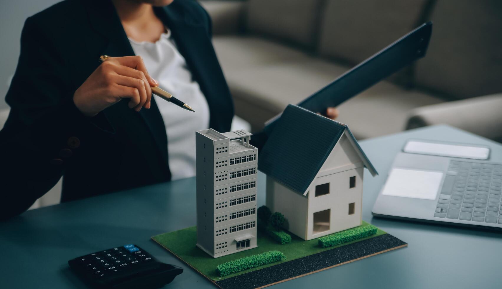 Close up realtor sit at table holds tiny house model, layout of cottage. Real estate purchase, new property, ownership, construction company make special offer to client, affordable dwelling concept photo