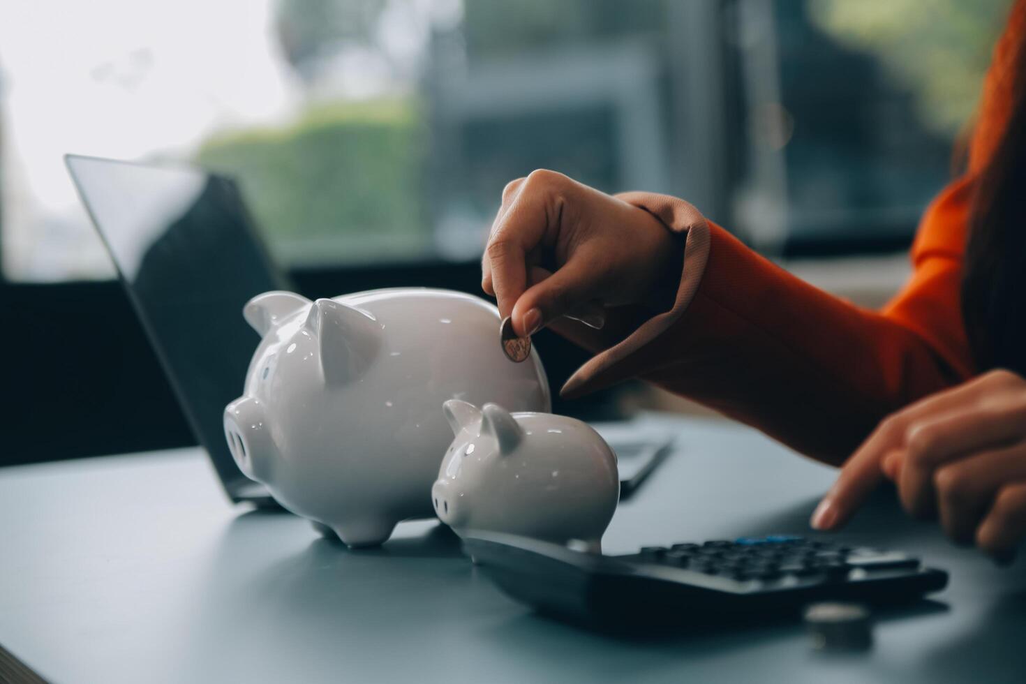 A young girl works at a laptop, writes a business development plan in a notebook, develops a strategy and makes calculations of earned funds. A woman puts her savings in a piggy bank. photo
