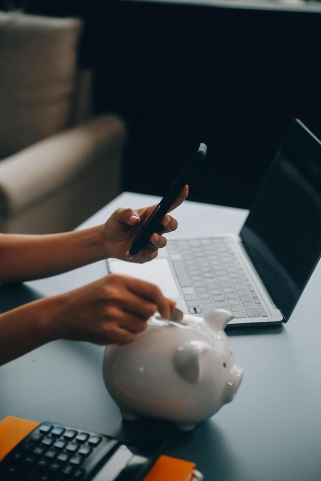 Young Asian woman saving for retirement Saving money through a piggy bank and taking notes on notebook, savings concept. photo