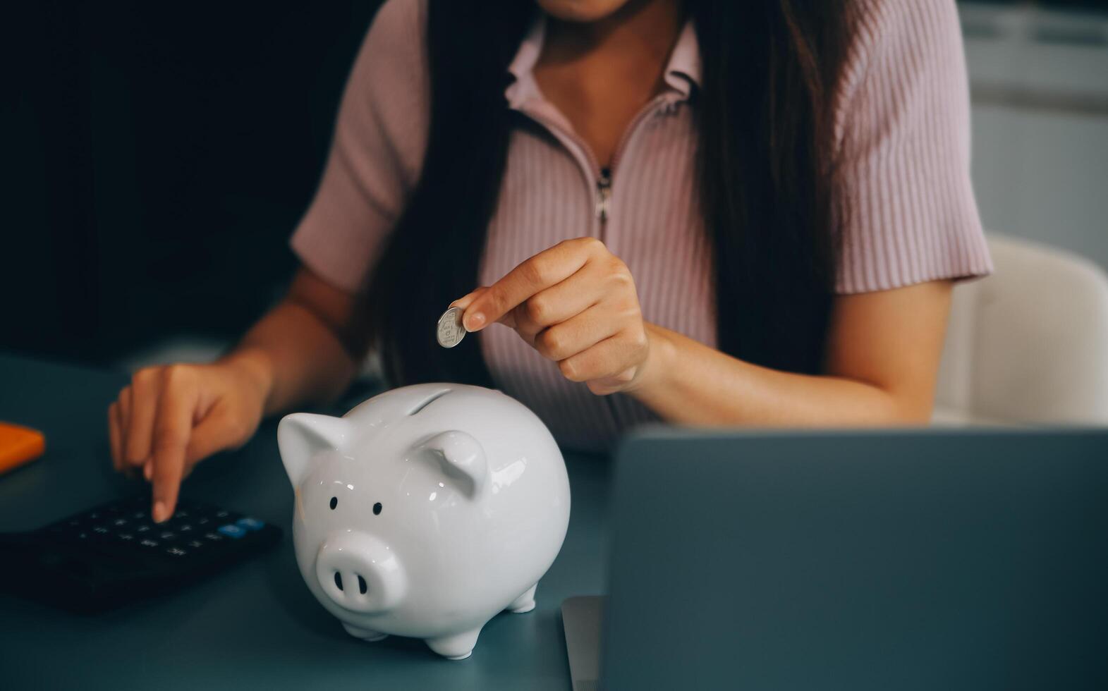 Young Asian woman saving for retirement Saving money through a piggy bank and taking notes on notebook, savings concept. photo