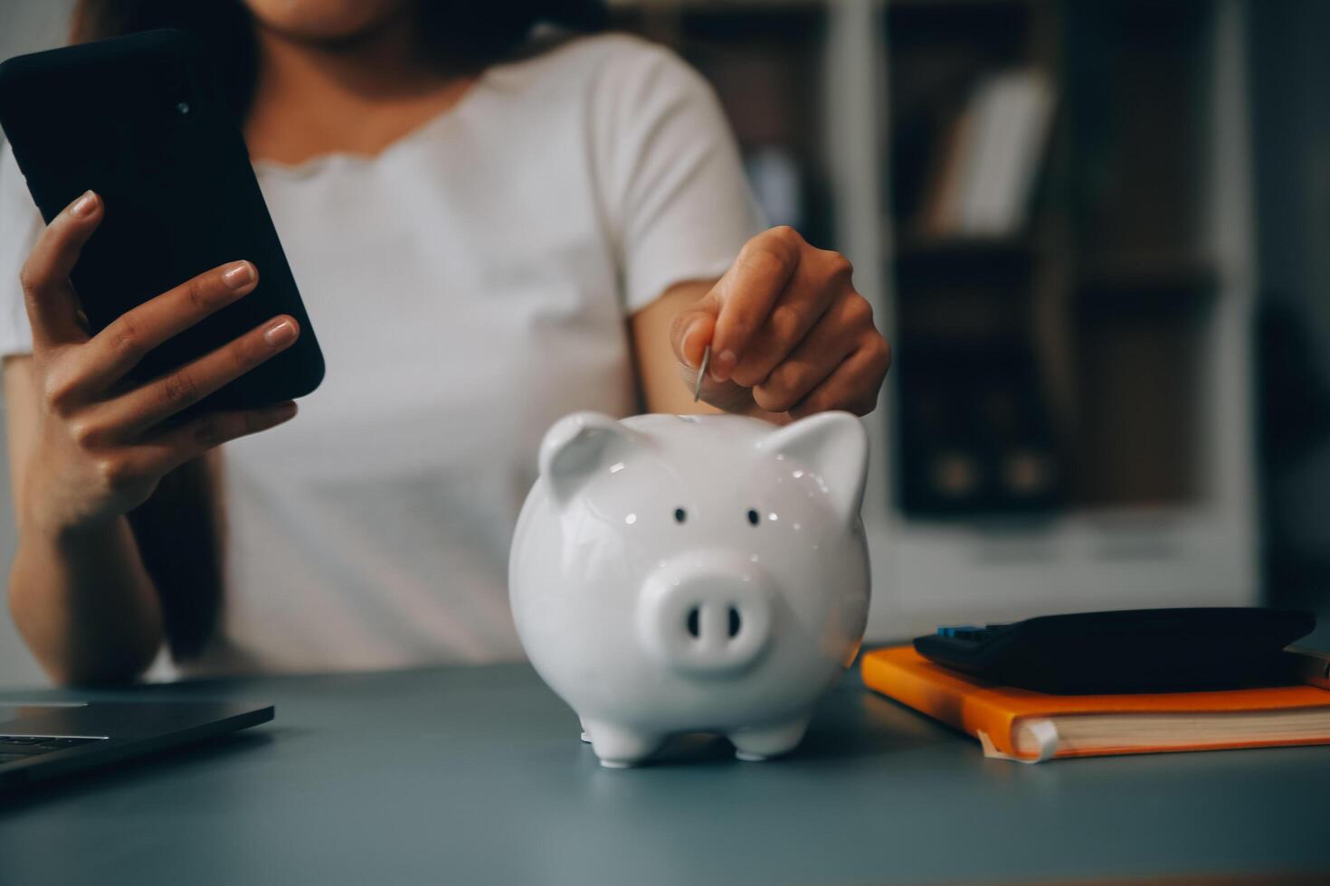 Young Asian woman saving for retirement Saving money through a piggy bank and taking notes on notebook, savings concept. photo