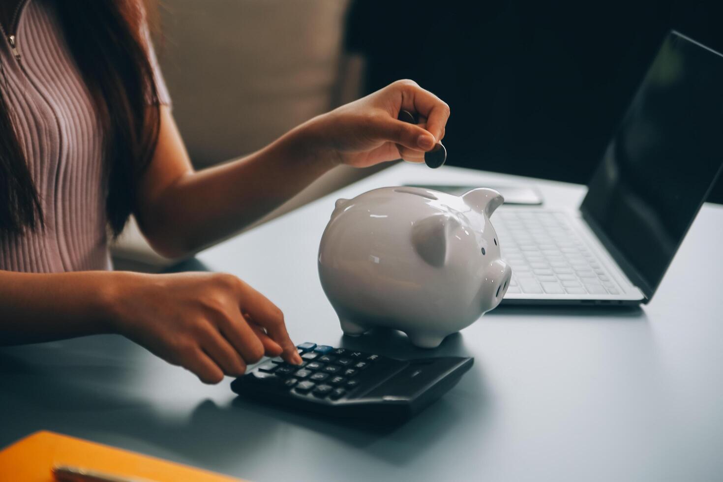 Young Asian woman saving for retirement Saving money through a piggy bank and taking notes on notebook, savings concept. photo