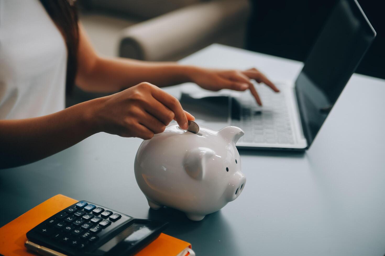 Young Asian woman saving for retirement Saving money through a piggy bank and taking notes on notebook, savings concept. photo