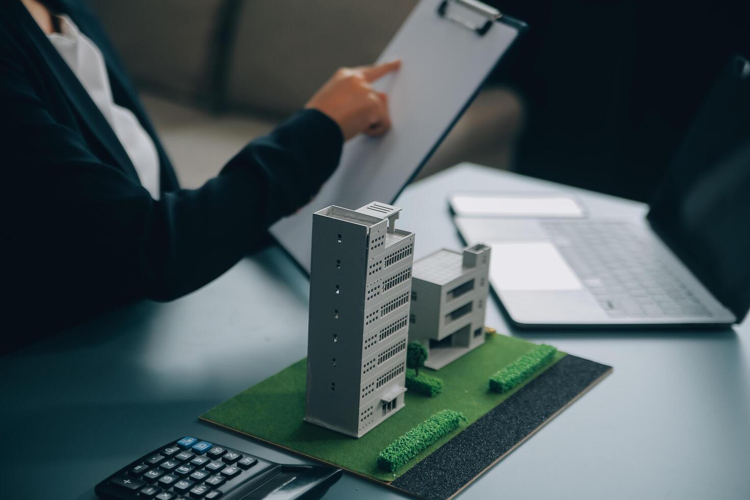 Close up realtor sit at table holds tiny house model, layout of cottage. Real estate purchase, new property, ownership, construction company make special offer to client, affordable dwelling concept photo