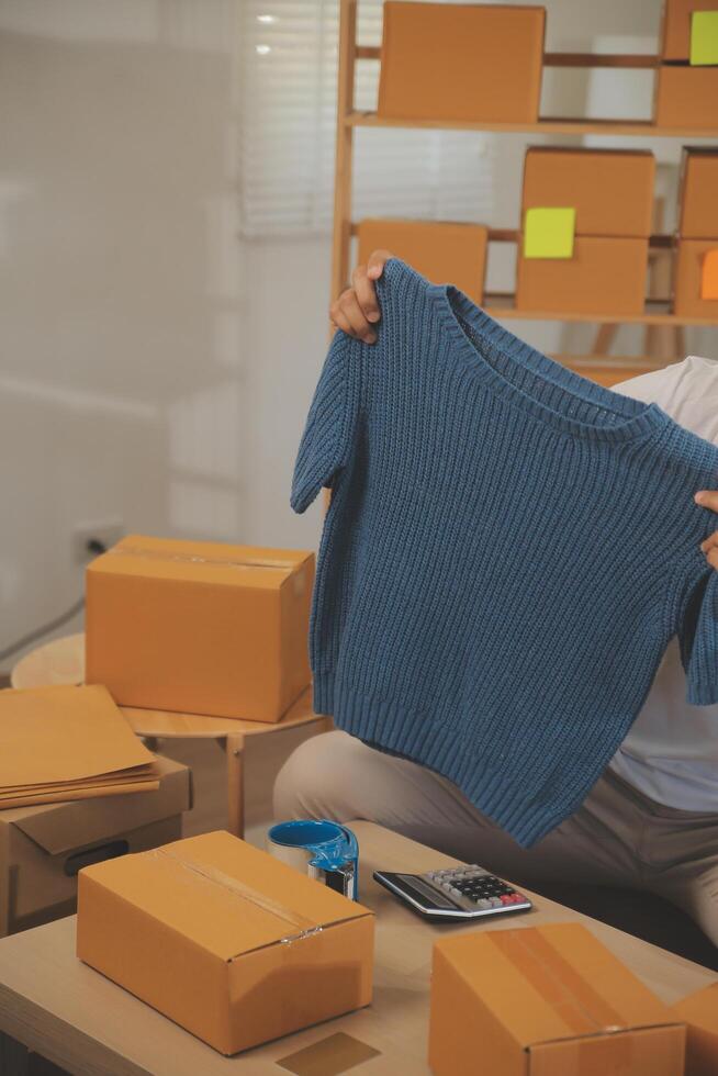 Two Asian blogger showing clothes in front of the camera to recording vlog video live streaming at her shop. Online Shopping Cart notion. on sofa at home photo