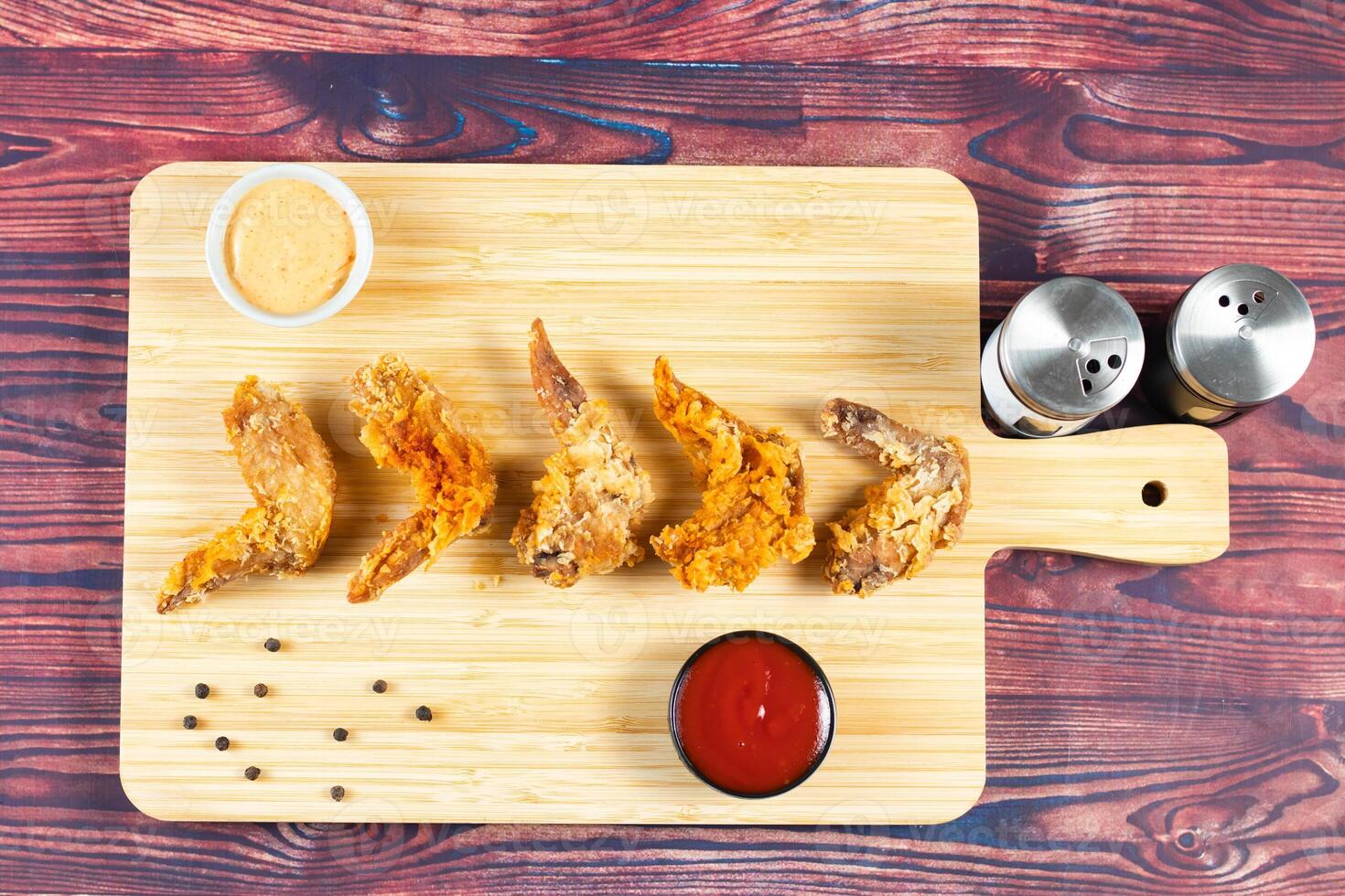 Crispy chicken wings with tomato sauce and mayo dip isolated on cutting board side view of fastfood photo